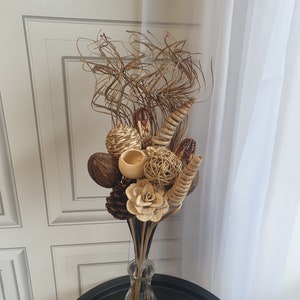 May include: A vase filled with a dried floral arrangement featuring brown, beige, and cream coloured natural elements, including pinecones, woven balls, and dried grasses.