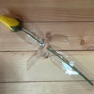 May include: A single yellow rose wrapped in clear cellophane with a sheer ribbon and a small rhinestone embellishment.