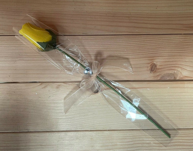 May include: A single yellow rose wrapped in clear cellophane with a sheer ribbon and a small rhinestone embellishment.