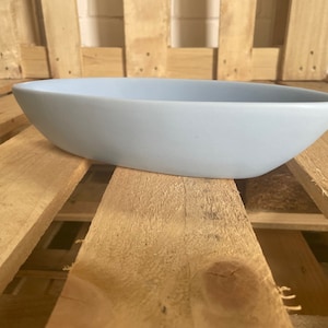 May include: A light blue ceramic planter shaped like a boat. The planter is sitting on a wooden surface.