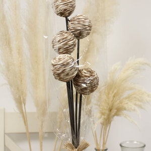 Peut inclure: Un bouquet de pampas séchées et de tiges de sphères tissées brunes et blanches dans un vase transparent avec un ruban en toile de jute.