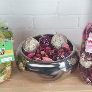 Peut inclure: Trois compositions de pot-pourri décoratives. Un bol argenté contient des fleurs séchées roses et beiges et des boules décoratives. Deux sacs en cellophane transparents contiennent du pot-pourri, l'un vert et beige, l'autre rose.
