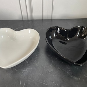Puede incluir: Dos cuencos de cerámica en forma de corazón, uno blanco y otro negro. Los cuencos están sobre una encimera gris.