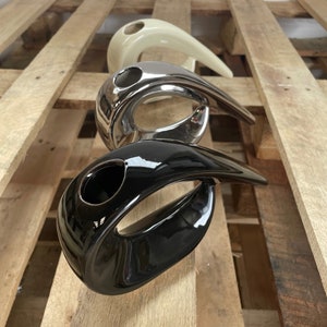 Pode incluir: Três vasos de cerâmica em diferentes cores: branco, prata e preto. Cada vaso tem uma forma abstrata única com um furo no centro para flores.