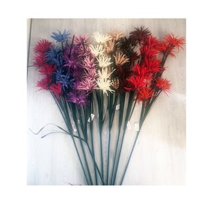 Op de afbeelding: Een boeket kunstbloemen met stelen. De bloemen zijn in tinten rood, roze, paars en crème. De bloemen zijn waaiervormig gerangschikt.