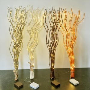 May include: Four decorative lighted branches in gold, cream, brown, and orange. Each branch is wrapped with tiny LED lights and bundled at the base. Battery packs are visible at the base of each branch, ready for use.