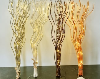 May include: Four decorative lighted branches in gold, cream, brown, and orange. Each branch is wrapped with tiny LED lights and bundled at the base. Battery packs are visible at the base of each branch, ready for use.