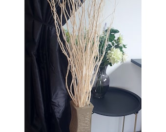 May include: A tall, brown, twisted ceramic vase filled with white twig branches. The vase is on a wooden floor in front of a black curtain.