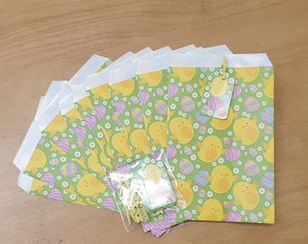 May include: A set of 10 small, white paper bags with a green, yellow, and purple chick and Easter egg pattern. The bags are decorated with a yellow chick and Easter egg design. The bags are perfect for holding small gifts or treats.