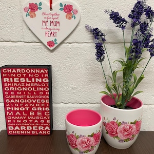 Può includere: Un ornamento a forma di cuore in ceramica bianca con fiori rosa e il testo "Close together or far apart MY MUM is always in my HEART". Due vasi di fiori in ceramica bianca con fiori rosa e una pianta di lavanda.