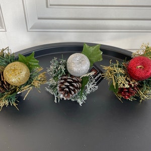 May include: Three Christmas ornaments, each with a different color and design. The first ornament is gold and has a pine cone design. The second ornament is silver and has a pine cone design. The third ornament is red and has a pine cone design.