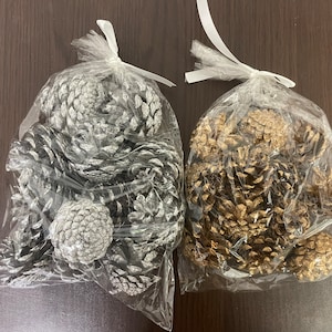 Puede incluir: Dos bolsas de piñas, una bolsa con piñas plateadas y una bolsa con piñas doradas.