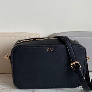 May include: Three crossbody bags, one in beige, one in black with the initials "GM" on the front, and one in light gray.