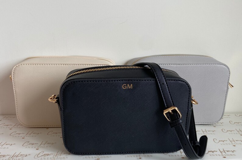 May include: Three crossbody bags, one in beige, one in black with the initials "GM" on the front, and one in light gray.