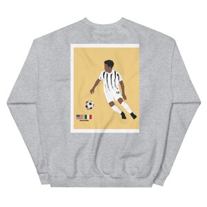 May include: A gray sweatshirt with a yellow background image of a soccer player in a white and black jersey with the number 14 on the back. The player is kicking a soccer ball. The image also includes the text "TEXAS BORN" and the flags of the United States and Italy.