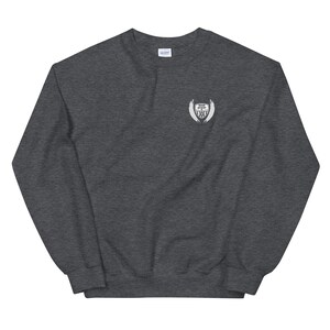 May include: A dark gray sweatshirt with a white embroidered patch on the left chest. The patch features a shield with wings and the text "Never Give Up The Fight".