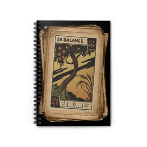 May include: A vintage-style spiral notebook with a black cover and a stack of old, worn, paper cards with a tarot card image on the top card. The card is labeled "20 BALANCE" and features a stylized image of a tree with fruit and wheat. The card has a scale symbol in the top right corner and bottom left corner.