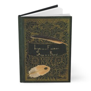 May include: A green journal with a gold floral design and the text "Light as a Feather, Stiff as a Board". Two feathers are depicted on the cover.