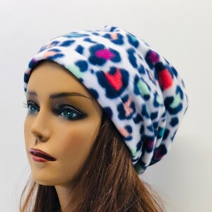 May include: A white beanie with a colorful leopard print pattern. The pattern includes dark blue, pink, red, and light green spots. The hat is made of a soft, possibly fleece, material.