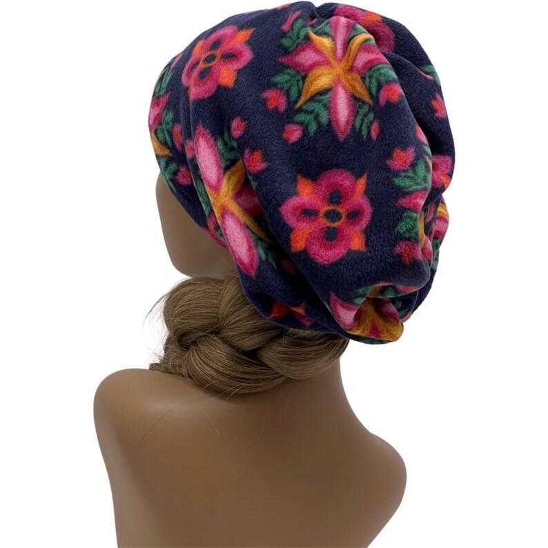 May include: A navy blue fleece beanie hat with a floral pattern in shades of pink, orange, and yellow. The hat is designed to be slouchy and comfortable, perfect for cold weather. The flowers are surrounded by green leaves.