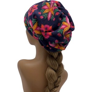 May include: A navy blue fleece hat with a floral pattern in shades of pink, orange, and yellow. The hat is a slouchy style, and the flowers have green leaves. The hat is displayed on a mannequin head.