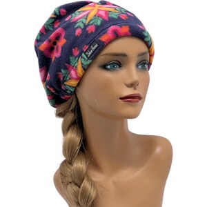 May include: A navy blue fleece beanie with a colorful floral pattern in pink, orange, yellow, and green. The beanie has a tag that reads "Deluxe Beanie".