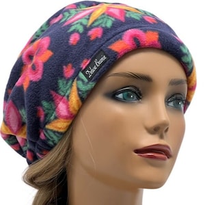 May include: Navy blue fleece beanie hat with a colorful floral pattern in pink, orange, yellow, and green. The hat has a tag that reads "Deluxe Beanie". This hat is a stylish accessory for cold weather.