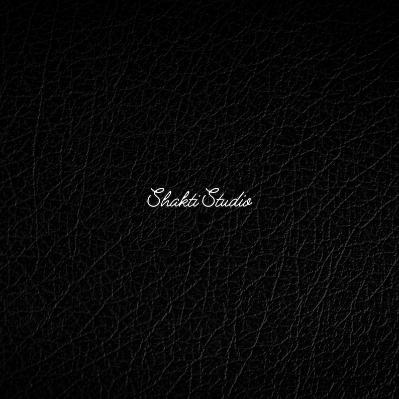 May include: A black surface with a textured, pebbled grain pattern resembling leather. Centered on the image is the text "Shakti Studio" written in a white, elegant, cursive script font that stands out against the dark background.