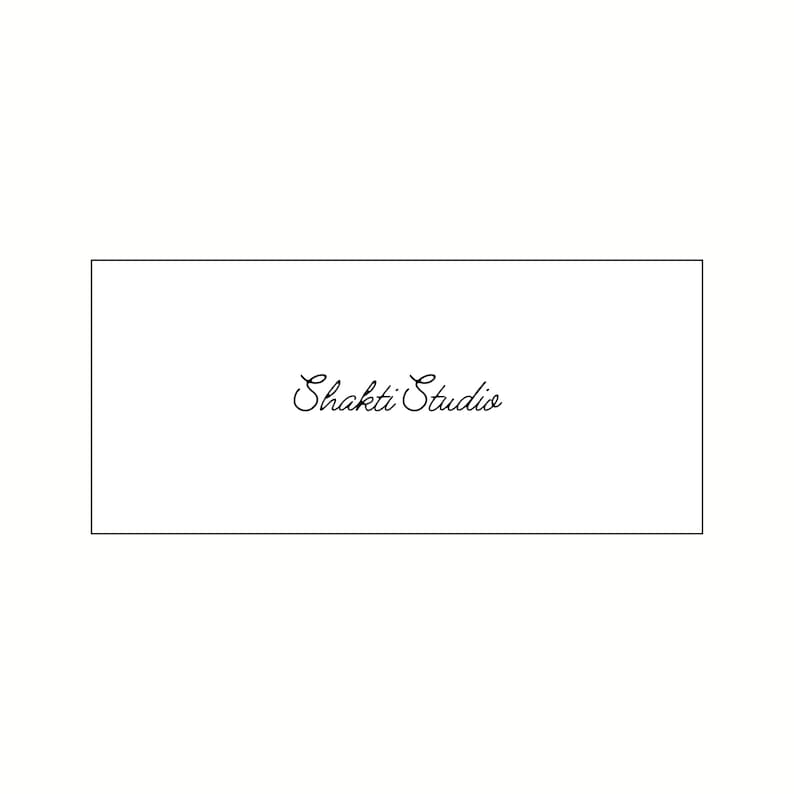 Op de afbeelding: Een witte rechthoekige kaart met de woorden "Shakti Studio" geschreven in elegant, cursief zwart schrift. De tekst is gecentreerd in de kaart, die is omlijnd door een dunne zwarte rand.