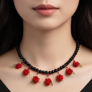Könnte beinhalten: Eine schwarze Perlenkette mit roten Rosenanhängern und grünen Blattakzenten. Die Halskette wird um den Hals getragen und ist ein auffälliges Schmuckstück.