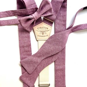 May include: A set of mauve-colored suspenders, a bow tie, and a self-tie bow tie. The suspenders have a cream-colored strap with metal hardware. The bow tie is pre-tied. The label reads "STRATTON SUSPENDER CO."