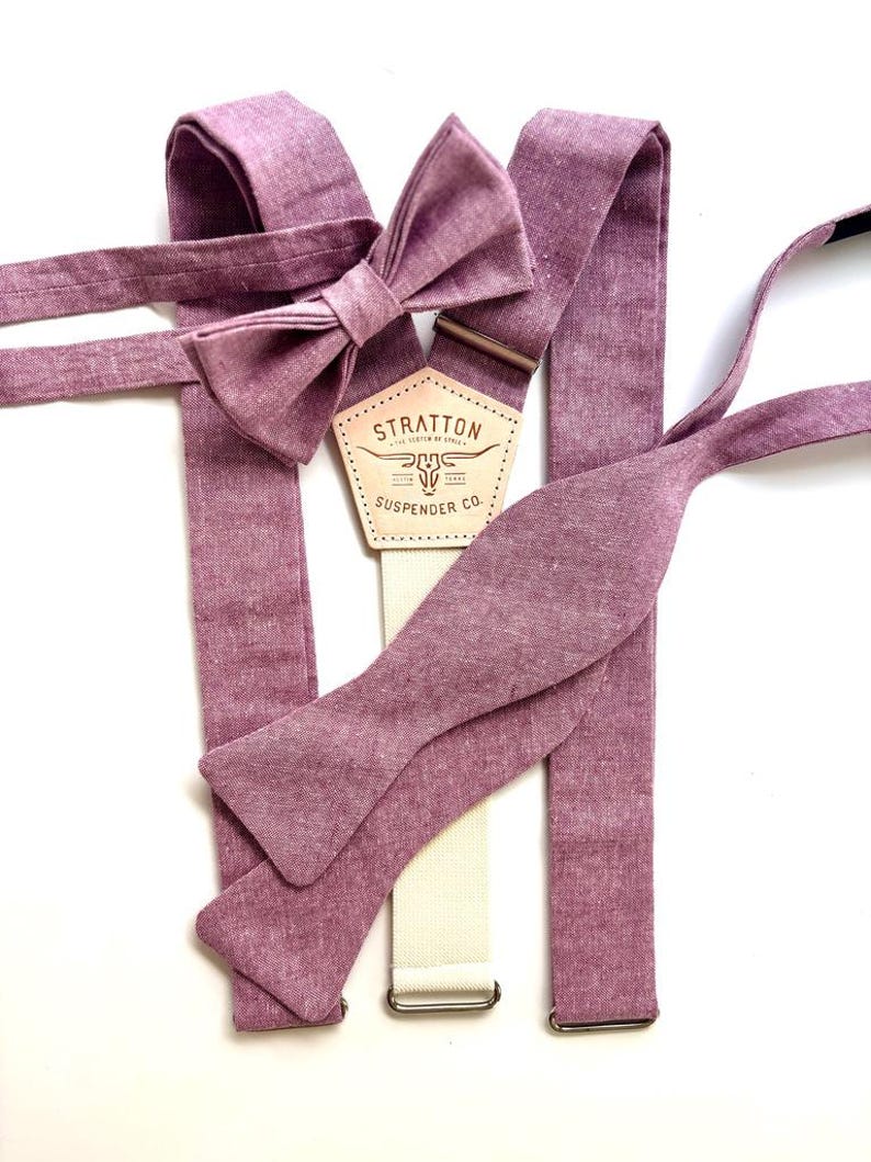 May include: A set of mauve-colored suspenders, a bow tie, and a self-tie bow tie. The suspenders have a cream-colored strap with metal hardware. The bow tie is pre-tied. The label reads "STRATTON SUSPENDER CO."