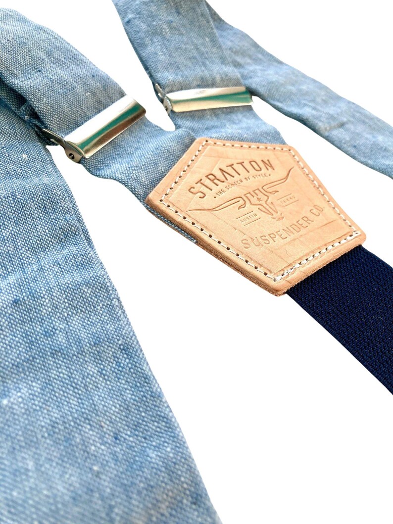 Light blue linen suspenders with navy elastic back strap and vegetable-tanned leather back patch. Handmade in Texas by Stratton Suspender Co. Perfect for weddings, groomsmen, and timeless menswear styles. Ethically made, premium-quality button suspenders.
