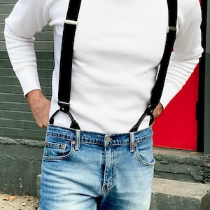Handmade black linen button-on suspenders for men, styled with denim jeans and a white waffle knit shirt. Classic and rugged groomsmen suspenders for weddings, vintage menswear, and timeless formal fashion. Ethically crafted in Texas, USA by Stratton Suspender Co.