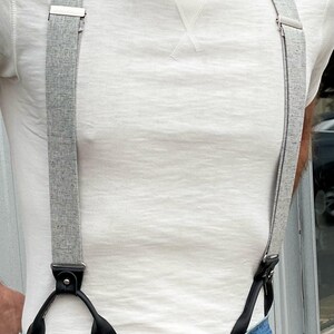 Men’s heather gray linen button-on suspenders paired with denim jeans and a classic off-white crewneck shirt. A perfect wedding and groomsmen accessory, these handcrafted suspenders blend vintage style with rugged craftsmanship. Ethically made in Texas by Stratton Suspender Co.