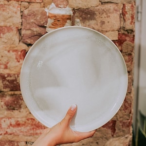 Könnte beinhalten: Ein weißer Keramikteller mit gesprenkelter Oberfläche. Der Teller wird von einer Hand gehalten.