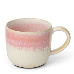 Pode incluir: Uma caneca grande de cerâmica de cor creme com um esmalte rosa degradê. A caneca tem uma base larga e arredondada e uma alça confortável.