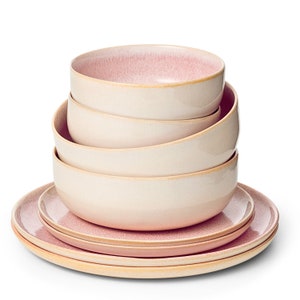 Può includere: Un set di quattro ciotole in ceramica rosa e crema impilate, con un piatto in ceramica rosa e crema sotto. Le ciotole sono annidate l'una dentro l'altra, con la ciotola più grande in basso e la più piccola in alto.