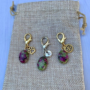 May include: Three gold-toned keychains with green and pink gemstone charms. Each charm has a different gold-toned accent: a paw print, a letter "R", and a number "69". The keychains are displayed on a brown burlap fabric.