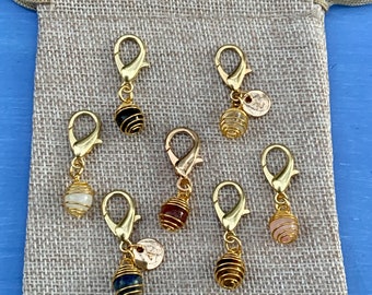 May include: Set of seven gold-tone stitch markers with different colored gemstone beads. Each marker has a small gold-tone charm attached.