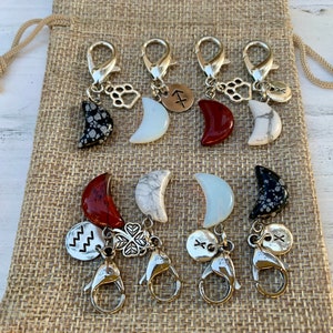 May include: Set of eight silver charm keychains with different moon-shaped stones, including red, white, and black. Each charm features a small silver charm with a symbol, such as a paw print, a clover, or a zodiac sign.