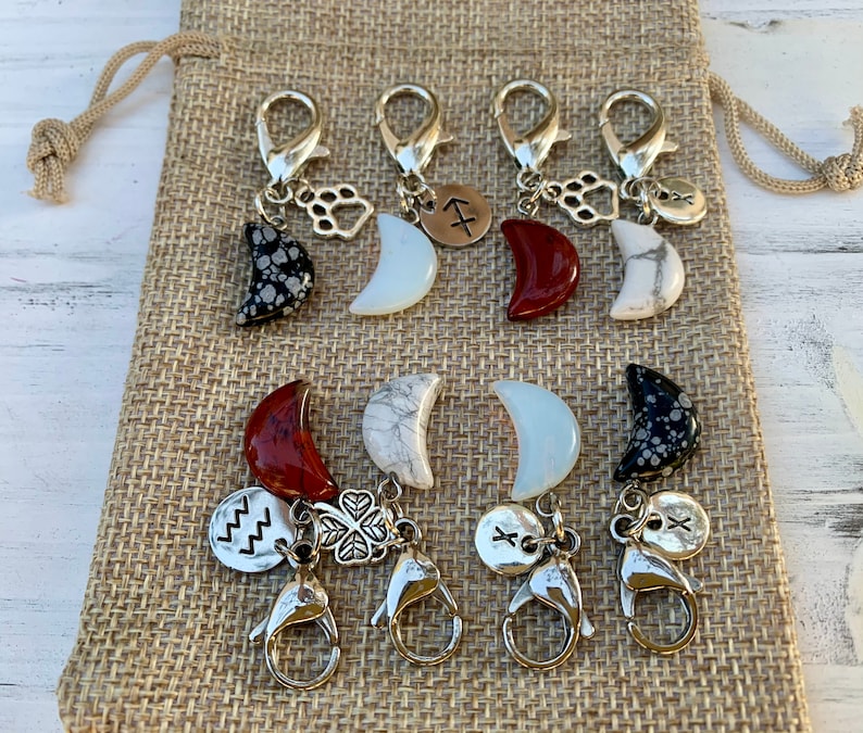 May include: Set of eight silver charm keychains with different moon-shaped stones, including red, white, and black. Each charm features a small silver charm with a symbol, such as a paw print, a clover, or a zodiac sign.