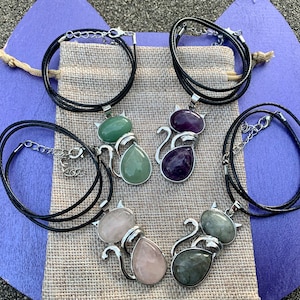 May include: Four silver cat necklaces with different colored gemstone pendants. The pendants are green, purple, pink, and gray.