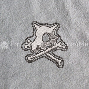 Puede incluir: Un parche bordado blanco de una calavera con huesos cruzados. La calavera es una representación de estilo de dibujos animados de un personaje Pokemon.