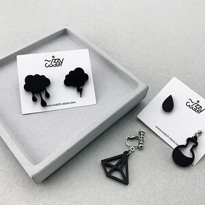 May include: Three pairs of black acrylic earrings. One pair features a cloud with raindrops, another pair features a cloud with a lightning bolt, and the third pair features a teardrop and a flask.
