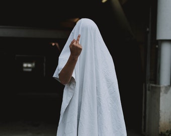 May include: A person wearing a white sheet over their head, with one hand raised in a middle finger gesture.