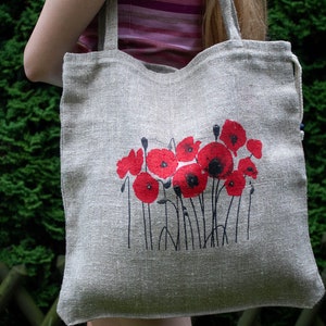 Può includere: Una borsa tote in lino beige con un disegno di papaveri rossi stampato sul davanti. La borsa ha due lunghi manici.