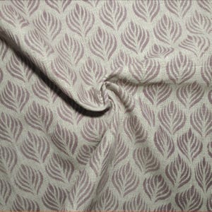 Op de afbeelding: Close-up van een stof met een herhaald patroon van gestileerde, mauvekleurige bladvormen op een lichtbeige achtergrond. De stof is licht gekreukt, wat de textuur en de drapering van het materiaal laat zien. Het bladerenpatroon is gelijkmatig verdeeld.
