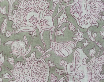 Op de afbeelding: Een groene stof met een wit en roze bloemenpatroon. De stof heeft een herhalend ontwerp van gestileerde bloemen en bladeren.