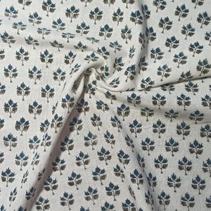 May include: White fabric with a repeating pattern of teal and brown stylized trees. The fabric is folded and textured.